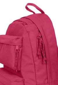 Mochila rosa con un tejido texturizado, múltiples compartimentos y cierres de cuerda ajustables. Incluye un asa en la parte superior.