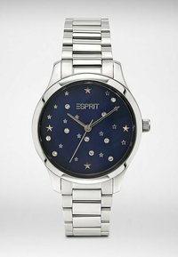 Silberne Metal Uhr mit einem blauen sternenbesäten Zifferblatt, das silberne Sterne und Kristalle als Stundenmarkierungen hat. Poliertes Armband mit Gliederdesign.