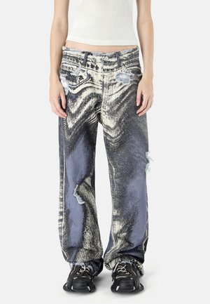 Jeans a gamba larga con motivo marmorizzato astratto in bianco e nero e dettagli consumati, indossati con sneakers nere e un top corto bianco.