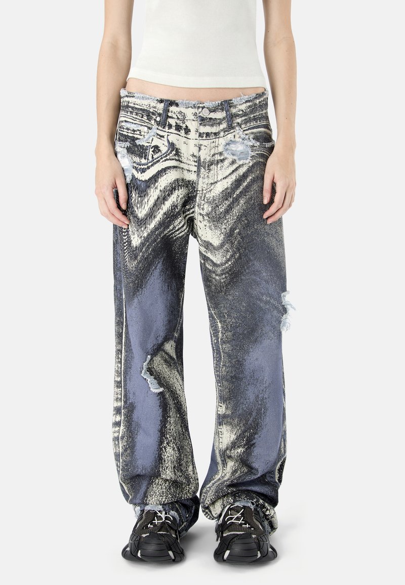 Jean à jambes larges avec un motif abstrait en marbre noir et blanc et des détails usés, porté avec des baskets noires et un crop top blanc.