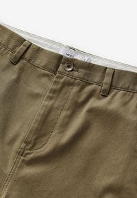Khaki chinos med en slät textur, dragkedjeförslutning, knappstängning och bältesloops; har en bakficka och subtila söm detaljer.