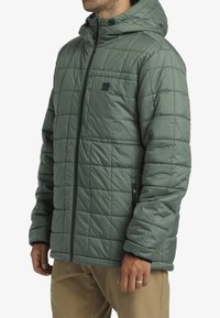 Quilted hooded jacket in olive green, featuring a full zipper, side pockets, and elastic cuffs, with a smooth, lightweight texture.