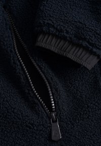 Veste en polaire bleu marine avec une surface texturée, dotée d'une fermeture éclair noire et de poignets élastiques pour un ajustement sûr.