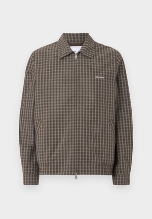 Pruun lukuga jakk valge ruudustikuga, terava kraega, küljetaskudega ja väikese valgete tikanditega tekstiga rinnal.