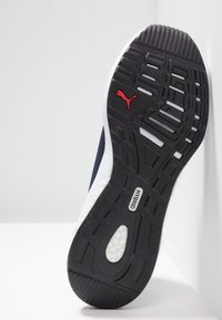 Sportovní obuv s texturovanou černou gumovou podrážkou, bílým mezipodešvem, modrou síťovinou na svršku a červeným logem Puma. Mezi designovými prvky je také hybridní systém tlumení.