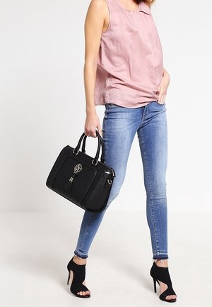 Woman wearing sleeveless pink top, blue skinny jeans, black open-toe heels, holding black handbag with decorative tassel.