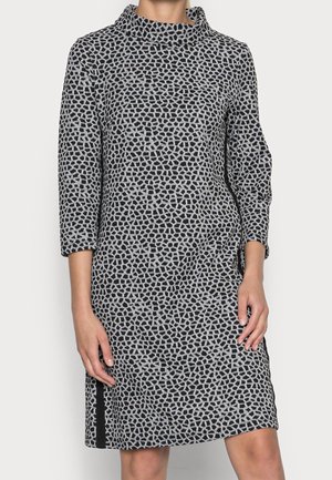 Woman wearing a knee-length black and gray patterned dress with three-quarter sleeves and a loose turtleneck collar.