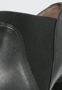 Botte de cheville noire en cuir lisse et tissu côtelé. Forme structurée avec un bout rond et sans quincaillerie visible.