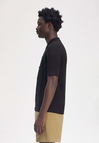 Camicia nera a maniche corte con bottoni, dalla linea dritta e con colletto, realizzata in un materiale morbido, abbinata a pantaloni beige.