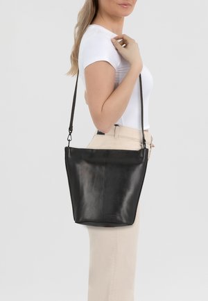 Schwarze Leder-Umhängetasche mit minimalistischem Design, flacher Form und verstellbarem Schulterriemen, vor einem neutralen Hintergrund präsentiert.