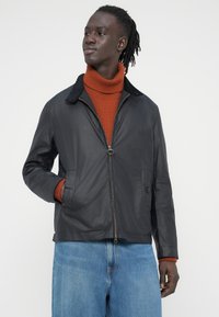 Μαύρο μπουφάν με φερμουάρ μπροστά, γιακά με εγκοπή και πλαϊνές τσέπες. Συνδυασμένο με πορτοκαλί ζιβάγκο με ριγέ υφή και φαρδιά τζιν παντελόνια σε ανοιχτό μπλε χρώμα.