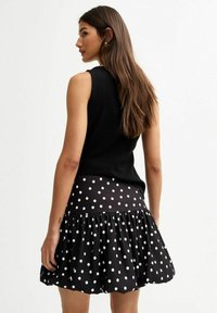 Un débardeur noir associé à une jupe à volants à pois, avec des pois blancs sur un fond noir, créant un contraste de motifs et de textures.