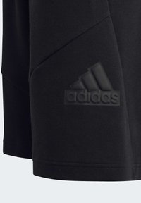 T-shirt nera in cotone con logo Adidas tonale sul lato sinistro in basso, con una texture liscia e un design a vestibilità rilassata.