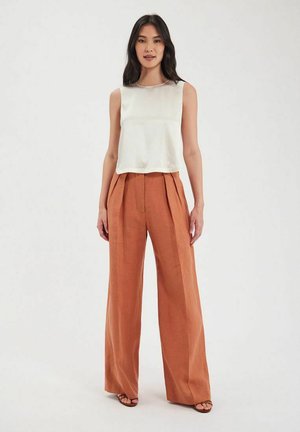 Haut sans manches blanc avec une finition lisse, associé à un pantalon en lin rouille à taille haute et à jambes larges avec des plis à l'avant.