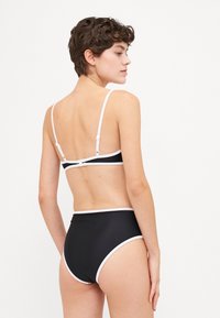 Fekete bikini szett fehér díszítéssel; a felsőrész állítható pántokkal és csattal záródik, míg a magas derekú alsórész sima textúrájú.