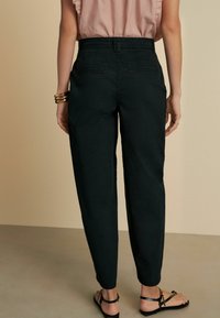 Sorte, tapered bukser med høj talje, der har to baglommer og et glat, let stof. Båret sammen med en rynket rosa top.