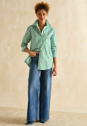 Green and white striped button-up shirt with a wide collar, paired with high-waisted, wide-leg blue jeans and teal pointed heels.