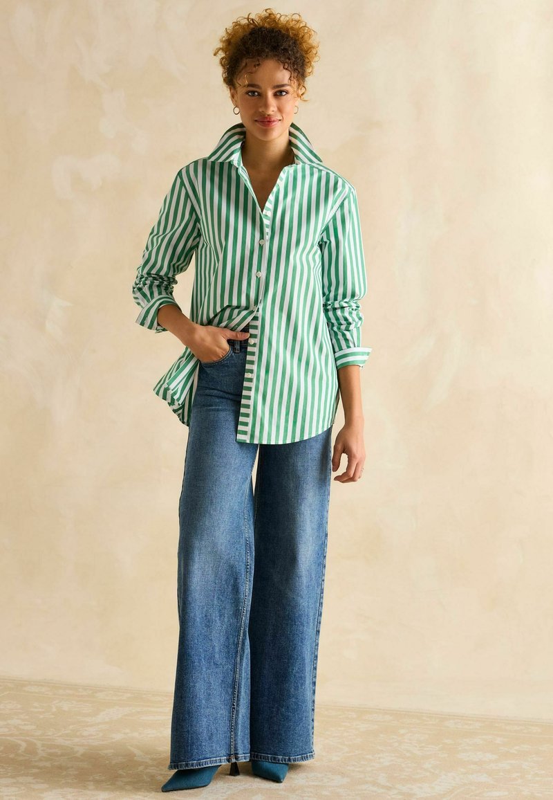 Grün-weiß gestreiftes Button-up-Hemd mit einem breiten Kragen, kombiniert mit hochgeschnittenen, weitbeinigen blauen Jeans und türkisfarbenen spitzen Absätzen.