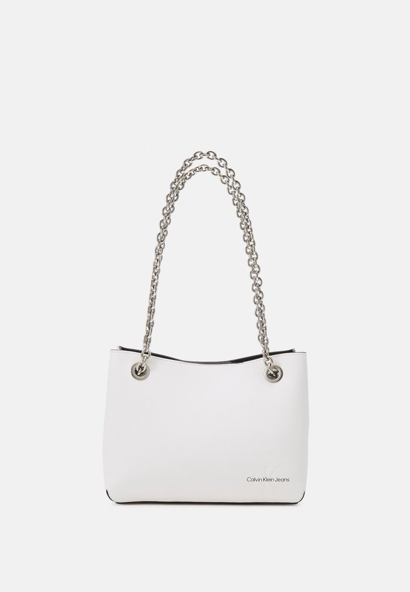 Bílá taška přes rameno z umělé kůže se stříbrným řetízkovým popruhem, s kovovými průchodkami a černým vnitřkem. Na přední straně je zobrazeno logo.