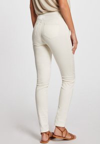 Jeans ajustados de color beige claro con una textura suave, bolsillos traseros con detalles de costura y una cintura de altura media.