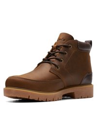 Bruine leren enkelboot met donkerbruine veters, gewatteerde kraag en dikke rubberen zool met profiel voor buitengebruik.