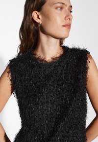 Zwarte mouwloze top met een textuur en een fuzzy afwerking. Heeft een ronde halslijn en een losse pasvorm. De gladde stofonderlaag is gedeeltelijk zichtbaar.