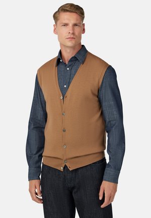 Chaleco de punto marrón con escote en V y cinco botones, usado sobre una camisa de manga larga de mezclilla oscura, combinado con jeans oscuros.