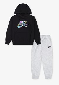 Črna kapuca z večbarvnim Nike logotipom, kenguru žepom in z vrvico ob kapuci, v kombinaciji s svetlo sivo trenirko z Nike logotipom.