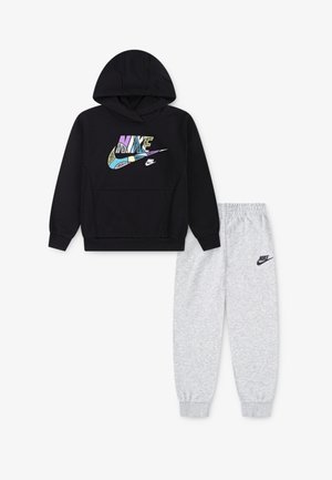 Crna dukserica s dužim rukavima i više boja Nike logotipom, s kengur džepom i kapuljačom na vezanje, uparenom s svijetlosivim trenirkama koje imaju Nike logotip.