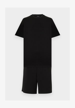 Fekete, rövid ujjú, kerek nyakú póló fekete, térdig érő rövidnadrággal, világosszürke egyszínű háttéren.