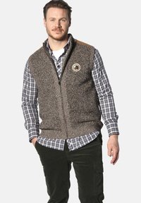 Brauner, gestrickter Weste mit Reißverschluss, die ein rundes Logo-Patch und beigefarbene Schulterakzente aufweist, getragen über einem karierten Hemd.