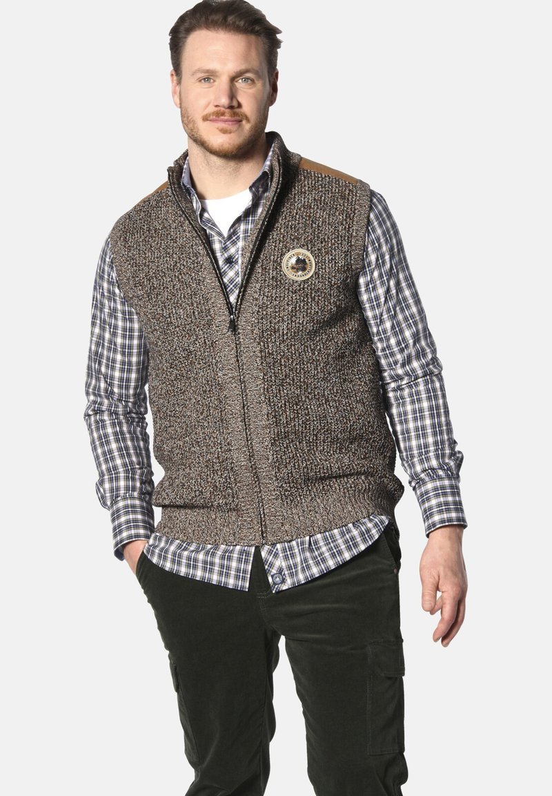 Brauner, gestrickter Weste mit Reißverschluss, die ein rundes Logo-Patch und beigefarbene Schulterakzente aufweist, getragen über einem karierten Hemd.