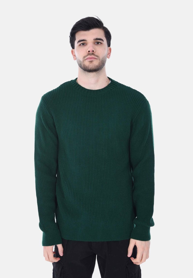 Maglione lavorato a maglia verde scuro con una texture a costine, colletto rotondo e maniche lunghe, abbinato a pantaloni neri.