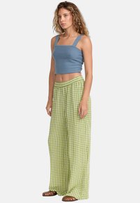 Ljusblå cropped top med en strukturerad yta och fyrkantig halsringning, tillsammans med lösa gröna rutiga byxor. Bruna sandaler fulländar hela outfiten.