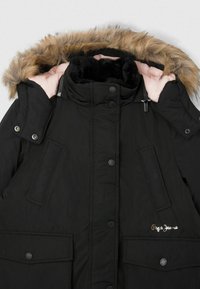 Černá parka s kapucí z kožešiny, patentkami, dvěma předními kapsami a vyšitým logem na hrudi. Vnitřní část má růžovou podšívku.