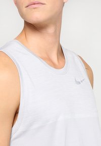 Canotta sportiva senza maniche grigio chiaro con una finitura texturizzata e un piccolo logo riflettente Nike sul petto, caratterizzata da un colletto tondo.