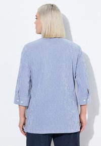 Camicia button-up a righe verticali blu e bianche. Presenta maniche a tre quarti con dettaglio dei bottoni, vestibilità rilassata e texture della stoffa morbida.