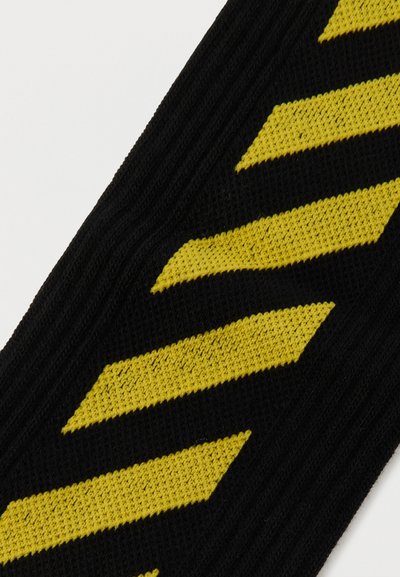 Μαύρο πλεκτό ύφασμα με γωνιακές κίτρινες ρίγες που σχηματίζουν ένα επαναλαμβανόμενο διαγώνιο μοτίβο.