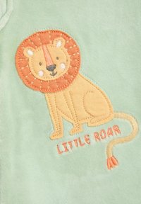 Der grüne Stoff zeigt einen gestickten Löwen mit einer strukturierten orangefarbenen Mähne, begleitet von dem Text "LITTLE ROAR" in Orange.