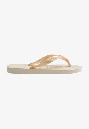 Beige flip-flop met een textuur voetbed, iets verhoogde zool en transparante banden met subtiele logo-embossing.