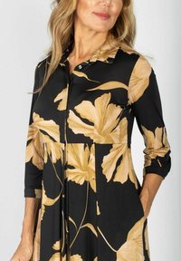 Czarna sukienka z dużym złotym kwiatowym wzorem, z kołnierzykiem, zapięciem na guziki i rękawami o długości trzech czwartych. Miękka tkanina o swobodnym kroju.