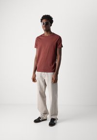Rudo crew-neck marškinėliai, lengvas audinys, derinami su pilkais laisvais džinsais ir juodais sportbačiais su baltais dryžiais. Papildyta akinių nuo saulės.