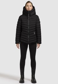 Giacca a vento nera con colletto alto, chiusura con zip e design a coste orizzontali. Abbinata a leggings neri e stivaletti.