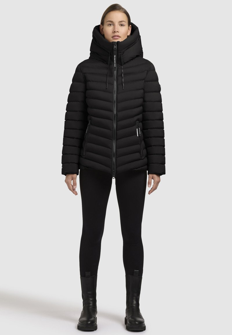 Giacca a vento nera con colletto alto, chiusura con zip e design a coste orizzontali. Abbinata a leggings neri e stivaletti.