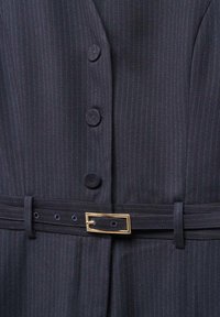 Veste de costume bleu marine à rayures fines, présentant un design épuré, six boutons et une ceinture assortie avec une boucle rectangulaire dorée.