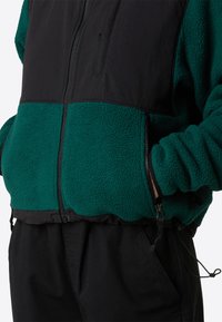 Giacca in pile zip-up verde e nera con materiale testurizzato, dotata di colletto rialzato e cordino regolabile in vita.