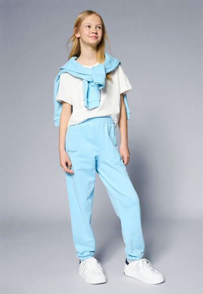 Pantalones de chándal azul claro con cintura elástica y puños, combinados con una camiseta blanca. Un suéter azul claro a juego está colocado sobre los hombros.