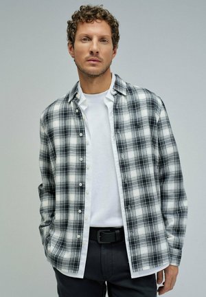 Camisa de cuadros en blanco y negro hecha de suave tejido de algodón, con un diseño de botones, mangas largas y un cuello clásico. Llevada sobre una camiseta blanca.