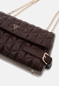 Sac à main en similicuir matelassé marron avec un logo triangulaire, des anses en chaîne dorée et un détail de boucle. Présente un motif texturé.