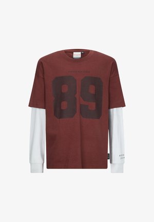 Korte mouwen bruine T-shirt met groot zwart nummer "89" en tekst, gelaagd over witte lange mouwen, katoenmix, ronde hals.